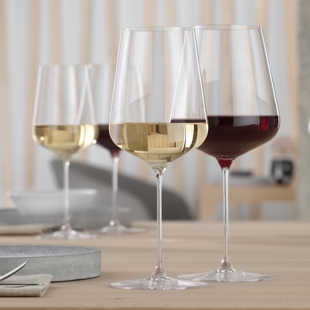 Un verre à bordeaux SPIEGELAU Definition rempli de vin rouge et un verre à vin blanc SPIEGELAU Definition rempli de vin blanc sur une table.